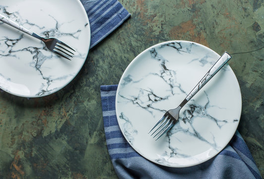 Empty Ceramic Plate With Fork And Blue Kitchen Towel Over Green Concrete Table Background. Top View With Copy Space. Flat Lay.