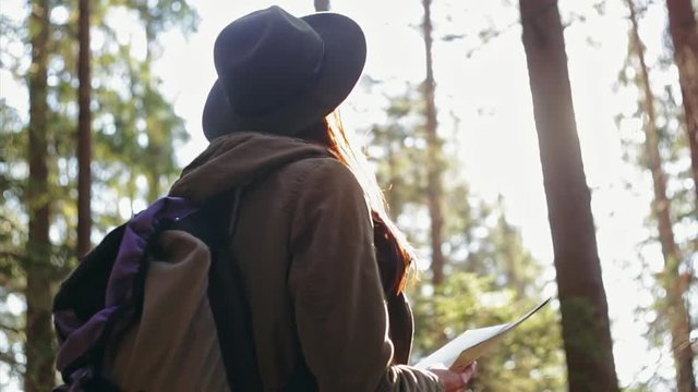 Stylish traveler girl in hat looking at map, exploring woods.