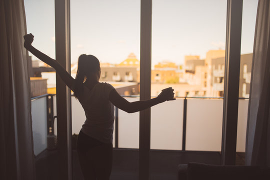 Sleepy woman stretching,drinking a coffee to wake up early in the monday morning sunrise.Starting your day.Wellbeing.Positive energy,productivity,happiness,enjoyment concept.Morning ritual