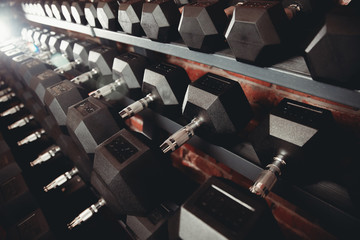 Lot of dumbbells stand in row in gym, glare of light. Concept slimming, musculature, bodybuilding,...