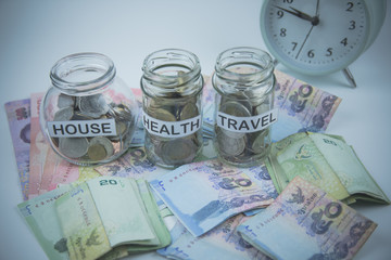 A lot coins in glass money jar on the white background Saving for house, health and travel concept.