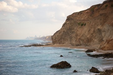 Fototapeta na wymiar A sandcliff on beach. Sea rocks in water. Thin beach strip near cliff. 