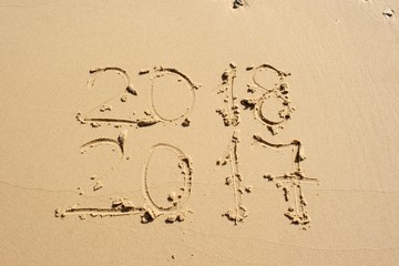 The new year is coming! 2018 and 2017 written in the sand one under the other.