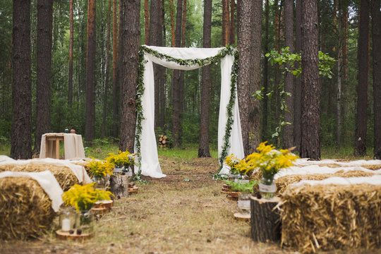 Beautifully decorated place in old autumn wood for wedding ceremony. Rustic style of elements of decor. Unusual seats made with straw. Horizontal color photography.