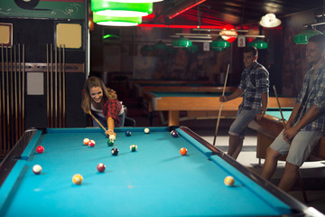 Young beautiful woman playing pool in a pub with her friends