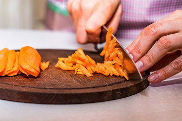 Woman's hands slice carrot on wooden board