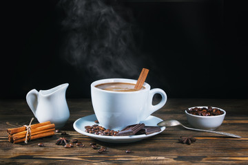 A cup of hot coffee with a cinnamon stick on a rustic wooden table on a dark background. Low key.