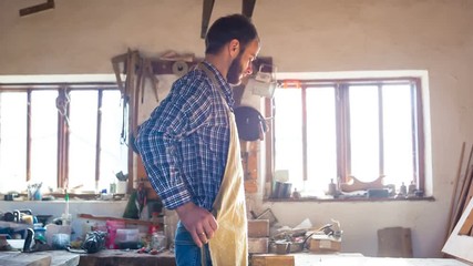 In a woodworking workshop, a young carpenter wears a protective apron