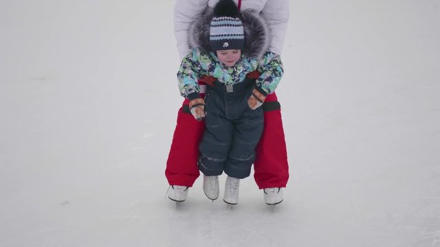 The first steps of a small child on ice skating. Mom teaches skating and holds his child on the ice. Active lifestyle