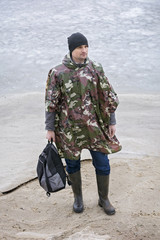 Young man walking on beach watching the frozen water in a military rain coat