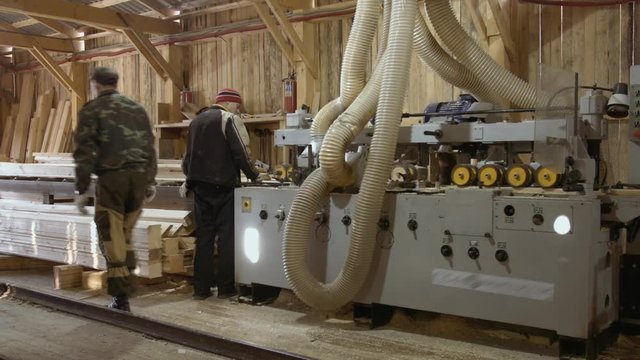 Joiners operates wood board running out carpenter jointer workbench at sawmill facility, lots of sawdust