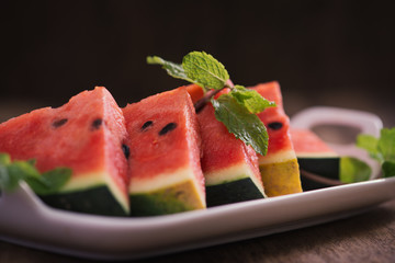 Fresh sliced watermelon in white dish on wooden table.