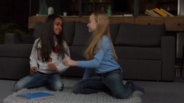 Little multiracial elementary girlfriends reconciling after quarrel and promise to be best friends forever in home interior. Cute girls hook each others fingers meaning to reconcile friendship at home