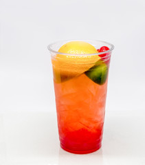 Fresh squeezed Fruit drink with an orange, Lime, and Maraschino Cherries in a clear cup on a white background.