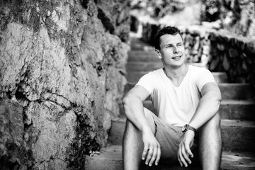 Portrait of a handsome charismatic guy sitting on the stairs. Black and white photo