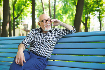 Obraz premium Smiling senior man in casual talking on mobile outdoors