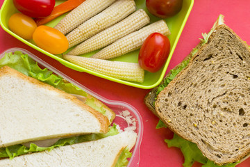 A set of lunch items: sandwiches and a green plastic container with vegetables, top view, close up, rose background