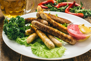 Chicken sausages with ketchup, mustard, beer, parsley, lettuce, on a white plate on a wooden table
