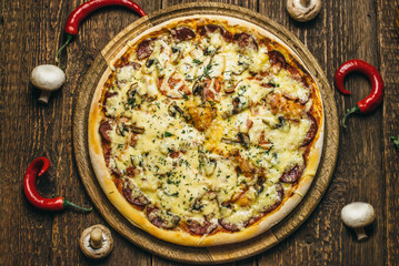 Delicious pizza with mushrooms, salami, cheese, tomatoes and pepper on a round wooden board on an old table. Top view