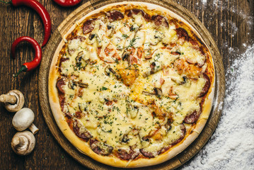 Delicious pizza with mushrooms, salami, cheese, tomatoes and pepper on a round wooden board on an old table. Top view