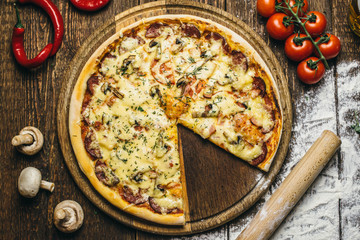 Delicious pizza with mushrooms, salami, cheese, tomatoes and pepper on a round wooden board on an old table. Top view