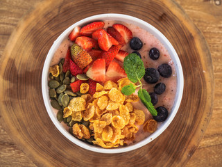healthy smoothie Bowl with cornflakes with fresh fruit like blueberries & strawberries on a wooden table from above