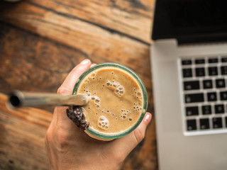 closeup of a laptop in a coffee shop on a wooden table with healthy avocado smoothie from top view