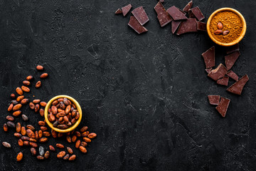 Chocolate and cacao concept. Cocoa powder in bowl near cocoa beans and broken chocolate on black...