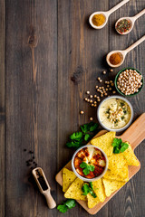 Serve hummus. Bowl with dish near pieces of crispbread on dark wooden background top view copy space