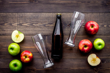 Apple cider. Low-alcoholic beveradge in dark bottle near beer glasses and fresh apples on dark wooden background top view copy space