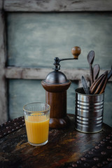 close up view of glass of juice, coffee grinder and cutlery on wooden surface