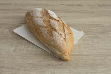 CRUSTY LOAF BREAD ON WHITE PAPER
Baked brown crusty french loaf on white paper, a whole loaf on the wood table.