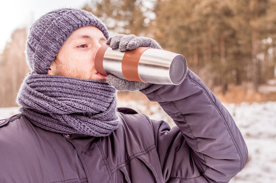 young man holds thermos in the woods in winter