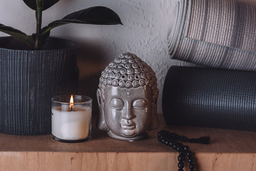 Sculpture of buddha head and yoga mats on wooden shelf