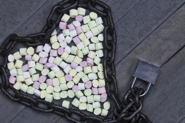 sweet marshmallows in heart shape decorated with chain and lock on wood background. valentine day concept.