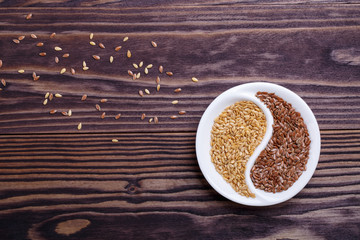 Golden and brown flax seeds on dark wooden background.