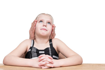 Naklejka premium Little girl sitting at table with closed hands with ears, isolated on white background