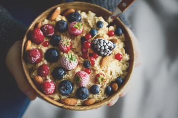 Girl hands holding oatmeal porridge with frozen berries, almonds in wooden bowl. Healthy breakfast. Clean eating, detox diet. Vegetarian, raw, vegan concept