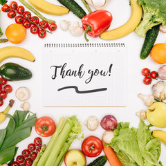 top view of notebook with words thank you between vegetables and fruits isolated on white