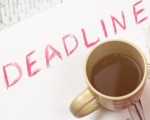 Deadline written on paper and a cup of coffee on scattered papers. Toned.