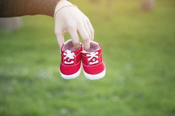 A portrait of a pregnant woman holding a pair of red sneakers baby shoes