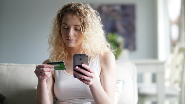 Beautiful blonde woman using credit card to shop online in a modern home interior