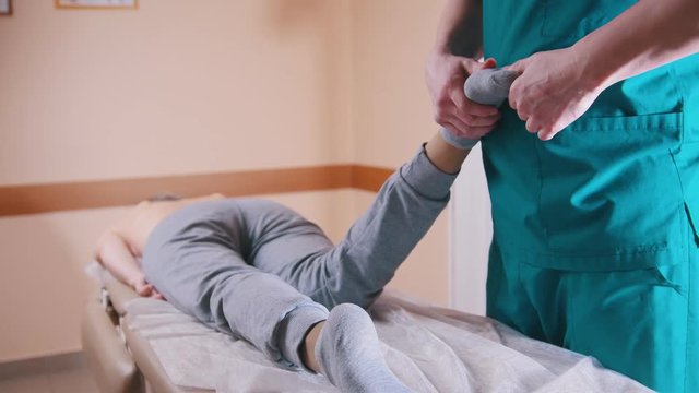 Chiropractor massaging a woman lying on a massage table, stretching and flexing her feet and knee, close-up of legs