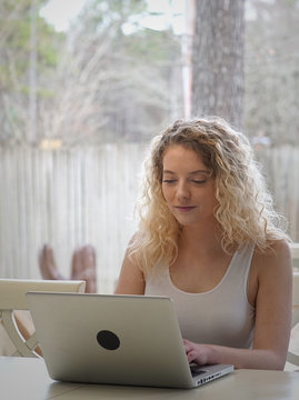 Beautiful Blonde woman works on laptop near a large window