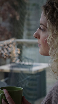 Depressed woman looks out window with green coffee cup