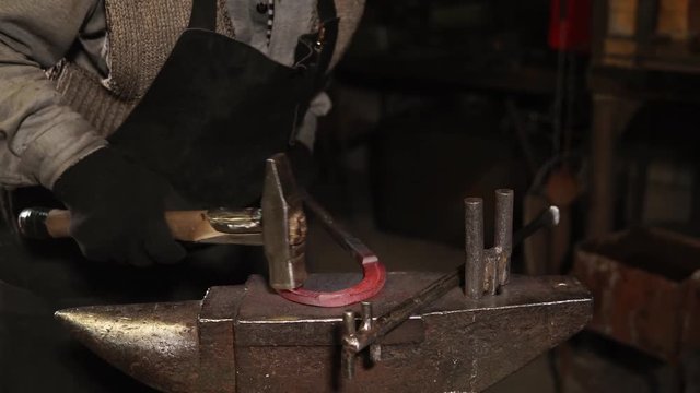 close up shot of a blacksmith's hands, a professional worker beats a hammer on the horseshoe, which was made of bent steel by several heated metal
