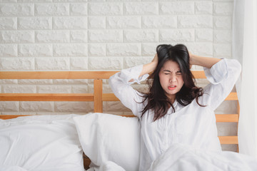 Unhappy young Asian woman wake up on her bed looking frustratedand and feeling sick.