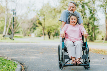 Happy smile Asian senior woman in a wheelchair relaxing and walking with her husband outside at the park