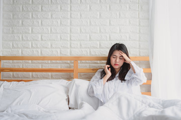 Attractive young Asian woman wake up on her bed looking unhappy and feeling sick.