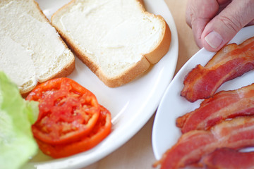 A man puts together a bacon, lettuce and tomato sandwich on white bread